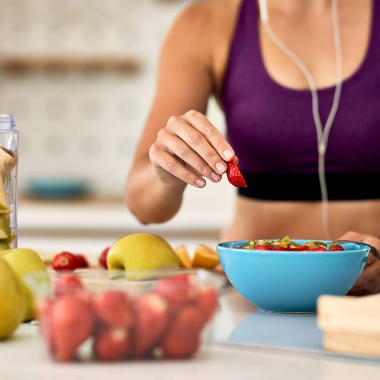 nutricion deportiva,primer plano de una mujer atlética añadiendo fresas mientras prepara una ensalada de frutas en la cocina